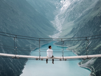 Man sitting on a footbridge spanning two mountains