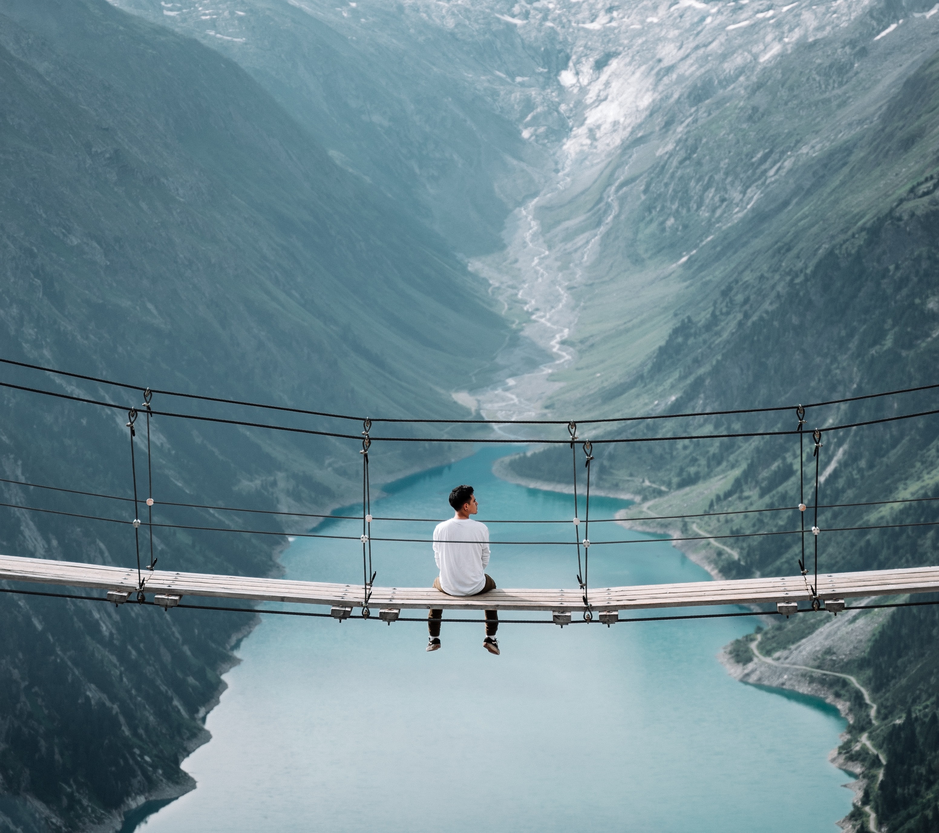 Man sitting on a footbridge spanning two mountains
